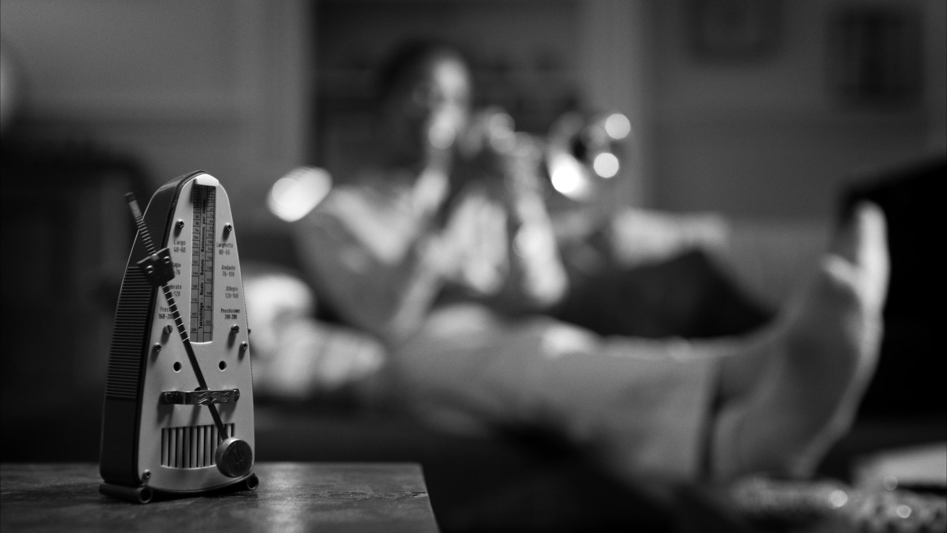 Grayscale background of a metronome on a table and a non-descript man playing a trumpet